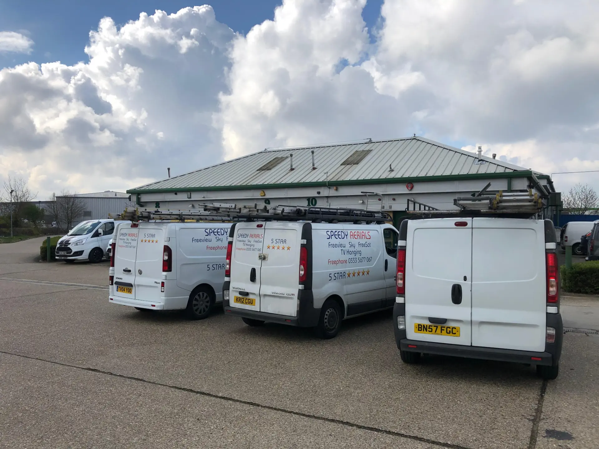 Speedy Aerials branded van fleet with roof-rack ladders parked at the Stevenage yard